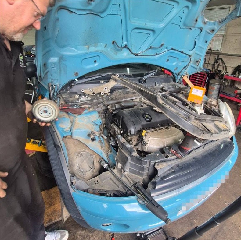 Working on the front end of a blue car with the bumper removed