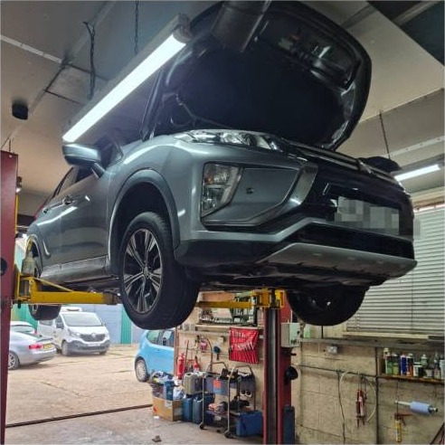 A grey SUV up on the lift with the workshop yard behind
