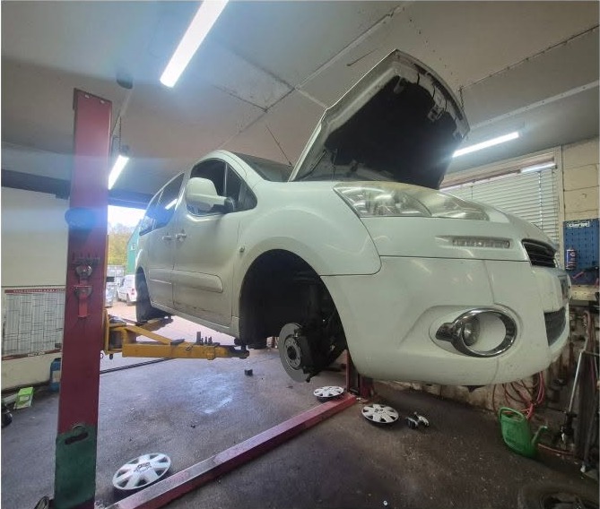 A white van on the lift with a front wheel off